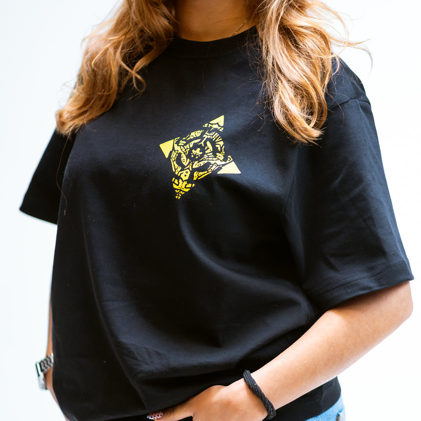 Person wearing a black Defqon.1 t-shirt with a yellow graphic design on a white background