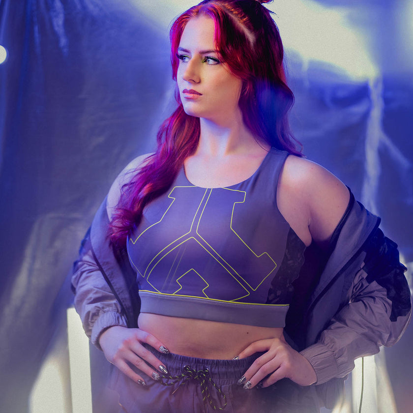 Woman wearing a Defqon.1 sports bra and shorts with a geometric design, standing against a blurred background.