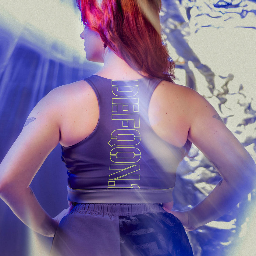 Person wearing a Defqon.1 tank top with 'DEEJAY' branding against a colorful abstract background