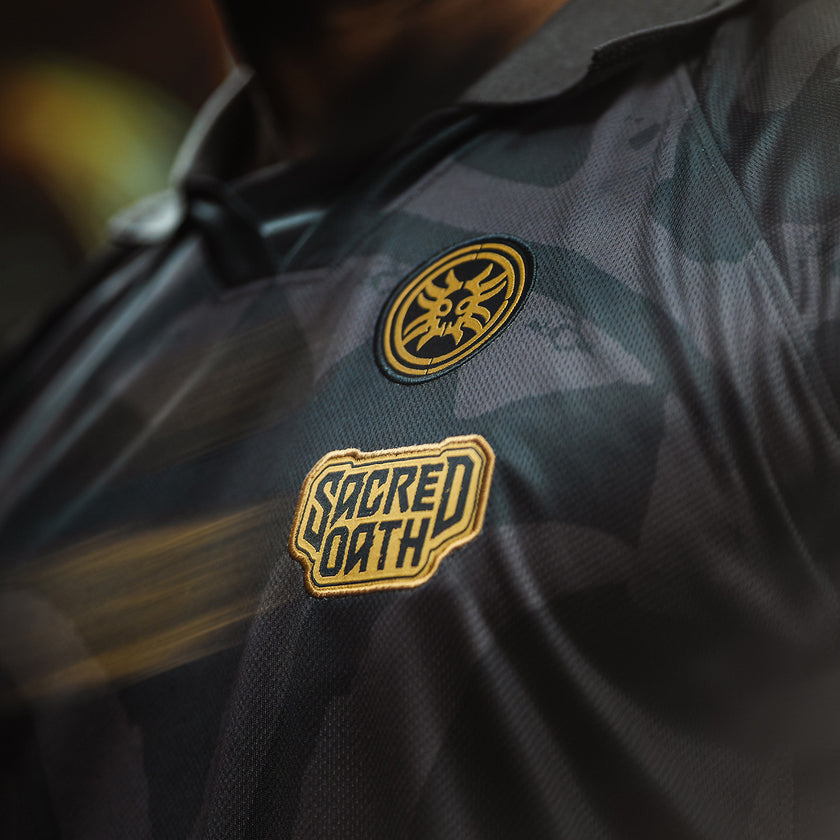 Close-up of a dark jacket with 'Sacred Oath' patches on a blurred background