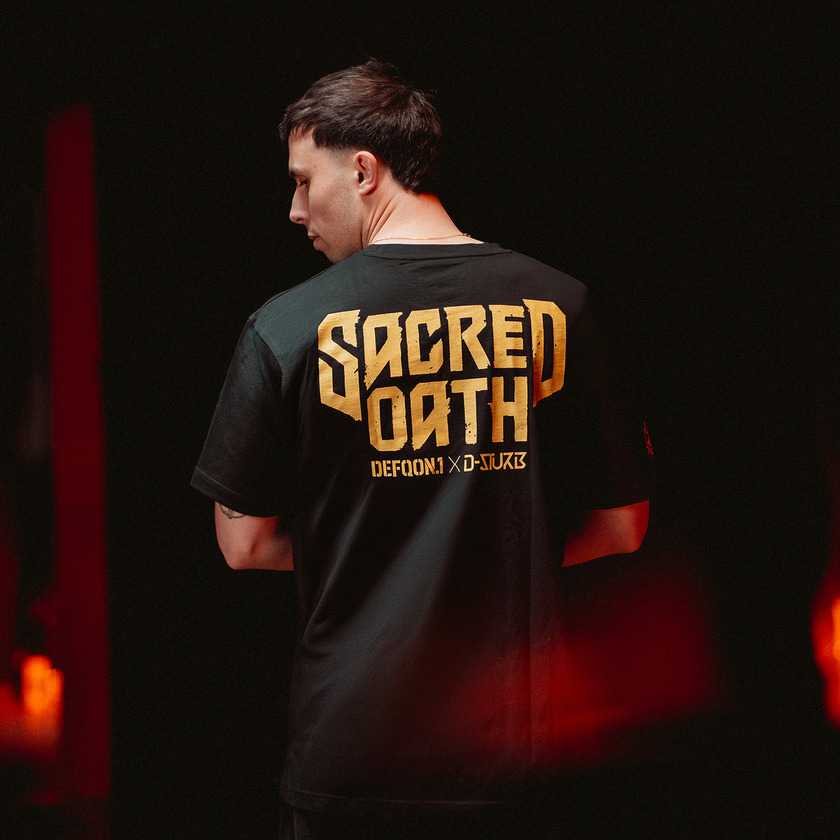 Person wearing a black Defqon.1 t-shirt with 'Sacred Oath' printed on the back in a dark setting.